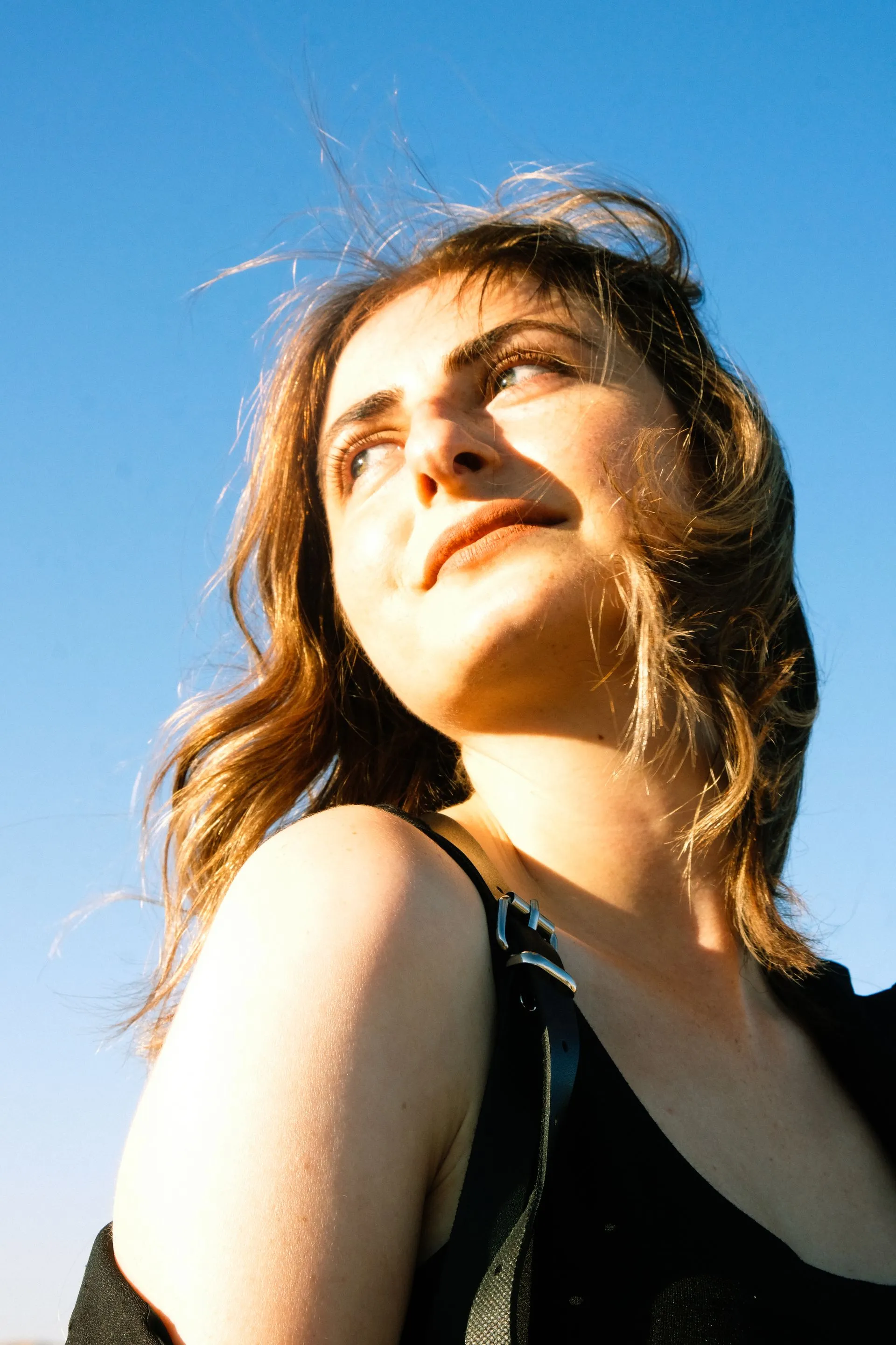 A woman outdoors looking up toward the sky in warm sunlight